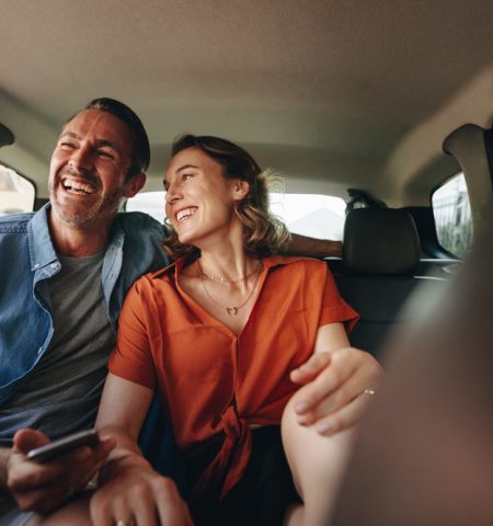 Two smiling passengers sitting in the back seat of a car