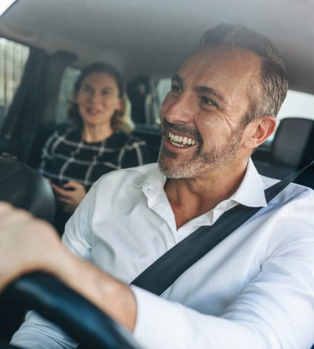 Smiling man driving a car with a passenger in the back seat